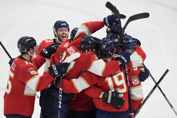 Florida Panthers center Sam Reinhart, far right, is mobbed by teammates after he scored during an overtime period of Game 4 during the Eastern Conference finals of the NHL hockey Stanley Cup playoffs to beat the New York Rangers, Tuesday, May 28, 2024, in Sunrise, Fla. (AP Photo/Wilfredo Lee)