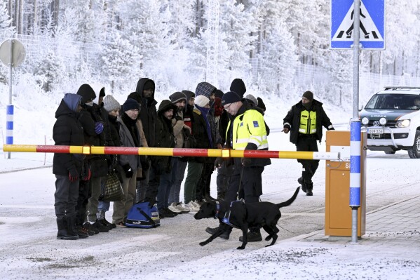 Migrants stare at a Finnish customs officer's dog at the Sala border crossing in northern Finland, Wednesday, November 22, 2023. (Jussi Nukari/Lehtikuva, via AP)