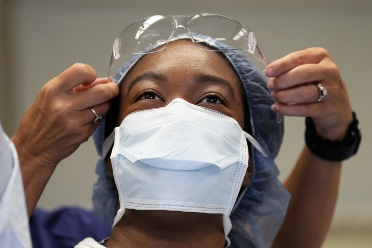 Meharry Medical College student Teresa Belledent gets help putting on her eye protection as she watches an organ procurement surgery June 15, 2023, in Jackson, Tenn. Belledent has long wanted to become a surgeon. She spent her childhood in Haiti and recalls family friends with kidney disease and no access to transplants. Specializing in transplant surgery “is definitely on the list because I like the idea of being able to give someone a second chance.” (AP Photo/Mark Humphrey)
