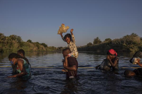 A little girl holds her stuffed animal high above the water as migrants, many from Haiti, wade across the Rio Grande river from Del Rio, Texas, to return to Ciudad Acuña, Mexico, Monday, Sept. 20, 2021, to avoid deportation. The U.S. is flying Haitians camped in a Texas border town back to their homeland and blocking others from crossing the border from Mexico. (AP Photo/Felix Marquez)