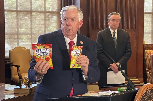 Missouri Gov. Mike Parson holds up an example of a legal package of Life Savers Gummies, left, and a slightly smaller package of hemp-derived gummies, right, at the Capitol in Jefferson City, Missouri. The hemp gummies will be banned under an executive order he issued prohibiting unregulated psychoactive cannabis products Thursday, Aug. 1, 2024. Mike Leara, right, supervisor of the state Division of Alcohol and Tobacco Control, will be responsible for making sure such products aren't sold at facilities with liquor licenses. (AP Photo/David A. Lieb)