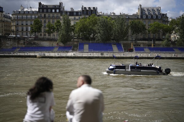 People sit along the Seine river with stands installed on its banks, Thursday, July 4, 2024 in Paris. The Seine river will host the Paris Olympic Games opening ceremony on July 26. (AP Photo/Thibault Camus)