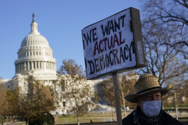 FILE - Protester David Barrows carries a sign during a rally to press Congress to pass voting rights protections and the "Build Back Better Act," Monday, Dec. 13, 2021, in Washington. A new poll finds that only about 1 in 10 U.S. adults give high ratings to the way democracy is working in the United States or how well it represents the interests of most Americans. (AP Photo/Patrick Semansky, File)