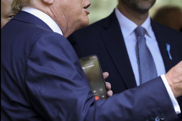 Republican presidential nominee former President Donald Trump holds his cell phone displaying Mike Johnson's name on a call while attending the 9/11 Memorial ceremony on the 23rd anniversary of the Sept. 11, 2001 attacks, Wednesday, Sept. 11, 2024, in New York. (AP Photo/Yuki Iwamura)