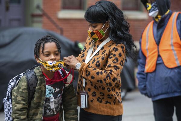 FILE - In this Monday, March 29, 2021, file photo, Jenea Edwards, of the North Side, helps her son Elijah, 9, in the third grade, with his mask before heading into Manchester Academic Charter School on the first day of in-person learning via a hybrid schedule, in Pittsburgh. Dozens of school districts around the country have eliminated requirements for students to wear masks, and many more are likely to ditch mask requirements before the next academic year.  (Andrew Rush/Pittsburgh Post-Gazette via AP, File)