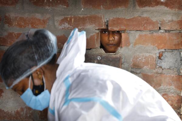 A girl looks out through a hole in the wall of her house as a health worker prepares for COVID-19 testing in Jamsoti village, Uttar Pradesh state, India, on June 9, 2021. India's vaccination efforts are being undermined by widespread hesitancy and fear of the jabs, fueled by misinformation and mistrust. That's especially true in rural India, where two-thirds of the country’s nearly 1.4 billion people live. (AP Photo/Rajesh Kumar Singh)