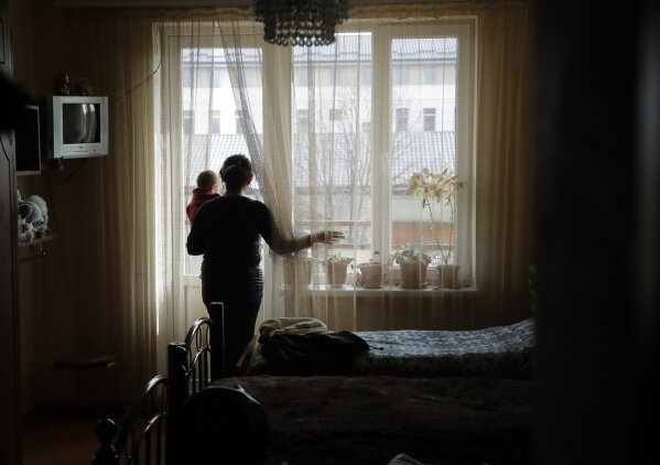 Ethnic Armenian refugee Bella Khachateryan holds her daughter Rita and looks through a window after returning to her flat in Stepanakert, the capital of the separatist region of Nagorno-Karabakh, on Tuesday, Nov. 17, 2020. Russian peacekeepers have started to move into the region, a total of 1,960 of them are to be sent in under a five-year mandate. Russia's Defense Ministry reported that the peacekeepers accompanied about 1,200 people returning to Nagorno-Karabakh from Armenia since Saturday. (AP Photo/Sergei Grits)