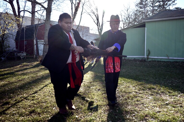 Anthony Yang, left, and Nhia Neng Vang , left, and Nhia Neng Vang mark a line representing the separation of the new year from the old with the blood of a rooster after a sweeping ritual in Nhia Neng Vang's backyard in St. Paul, Minn. on Saturday, Nov. 18, 2023. New Year is the most important traditional spiritual celebration for the Hmong refugees who settled here after fleeing in the aftermath of the Vietnam War. (AP Photo/Mark Vancleave)