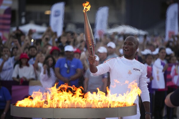 Torchbearer Didier Drogba of France holds the torch to light the cauldron at the Velodrome stadium in Marseille, southern France, Thursday, May 9, 2024. Torchbearers are to carry the Olympic flame through the streets of France's southern port city of Marseille, one day after it arrived on a majestic three-mast ship for the welcoming ceremony. (AP Photo/Daniel Cole)