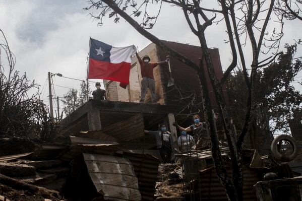 A resident holds up a Chilean flag from the shell of a home burned down by a forest fire, in Vina del Mar, Chile, Sunday, Feb. 4, 2024. (AP Photo/Cristobal Basaure)