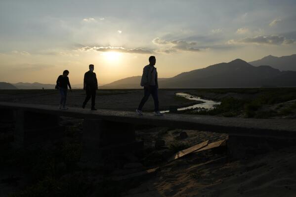 Residents walk along a stretch of dried up Poyang Lake as the sun sets in north-central China's Jiangxi province on Monday, Oct. 31, 2022. A prolonged drought since July has dramatically shrunk China’s biggest freshwater lake, Poyang. (AP Photo/Ng Han Guan)