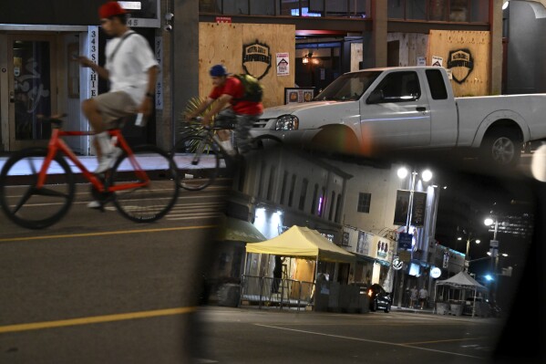 Bicycle riders cruise past boarded up businesses along 1st St. in Little Tokyo Tuesday, June 17, 2025, in Los Angeles. (AP Photo/Wally Skalij)
