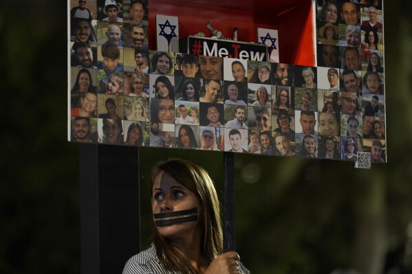 A person holds a placard with pictures of hostages held in the Gaza Strip, in a show of solidarity, in Tel Aviv, Israel Saturday, Nov. 25, 2023. Egyptian officials said Hamas was preparing to release 14 Israeli hostages Saturday for 42 Palestinian prisoners held by Israel. (AP Photo/ Leo Correa)