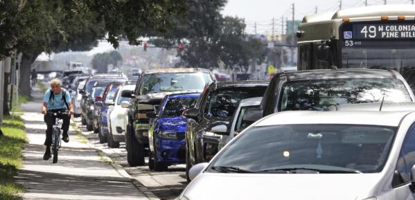 A cyclist passes cars at a standstill along West Colonial Drive in Orlando, Fla., Thursday, July 29, 2021, as residents wait in line for COVID-19 testing at Barnett Park. The line stretched through the park for more than a mile to the entrance to the Central Florida Fairgrounds. Orange County is under a state of emergency as coronavirus infections skyrocket in Central Florida. The Barnett Park site is testing 1,000 people a day and has closed early in recent days due to reaching capacity. (Joe Burbank/Orlando Sentinel via AP)