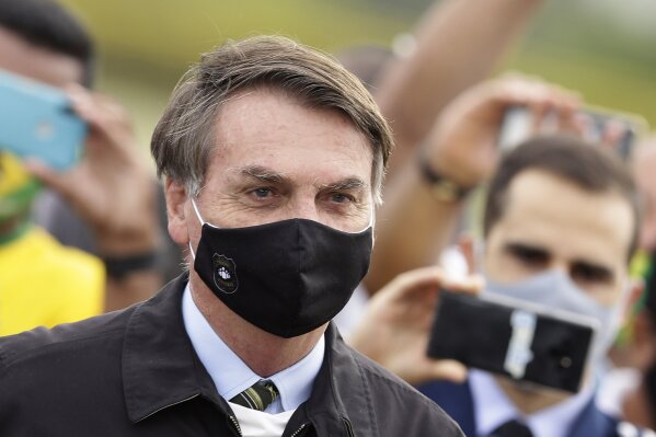 FILE - In this May 25, 2020, file photo, Brazil's President Jair Bolsonaro, wearing a face mask amid the coronavirus pandemic, stands among supporters as he leaves his official residence of Alvorada palace in Brasilia, Brazil. Bolsonaro said Tuesday, July 7, he tested positive for COVID-19 after months of downplaying the virus's severity while deaths mounted rapidly inside the country. (AP Photo/Eraldo Peres, File)