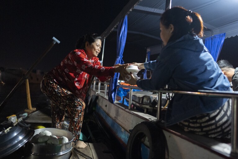 Nguyen Thi Thuy, a vendor selling steamed buns on a floating market, hands two to a tourist visiting from the U.S. in Can Tho, Vietnam, Wednesday, Jan. 17, 2024. On good days she makes about $4 — hardly enough to put food on the table. (AP Photo/Jae C. Hong)