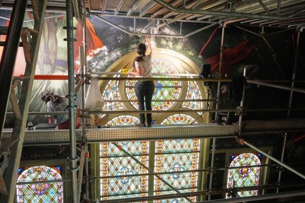 Standing on a 32-foot-tall scaffold, conservation technician Celeste Parrendo works on touching up a mural by Maxo Vanka inside St. Nicholas Croatian Catholic Church in Millvale, Pa., Monday, May 19, 2025. (AP Photo/Gene J. Puskar)