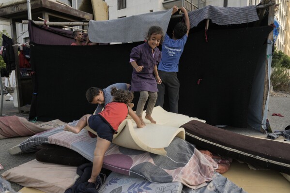 Children play as their father, left, set up a tent as temporary shelter after fleeing the Israeli airstrikes in Dahiyeh, Beirut, Lebanon, Monday, Oct. 14, 2024. (AP Photo/Bilal Hussein)