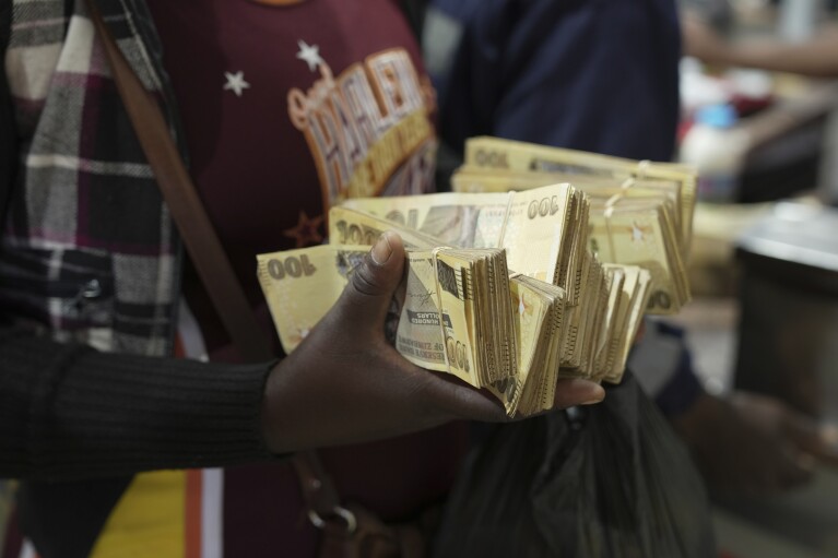 A woman uses old Zimbabwean dollar notes to buy groceries in a supermarket in Harare, Thursday, April 25, 2024. Zimbabwe started circulating banknotes and coins for another new currency Tuesday in its latest attempt to solve a long-running monetary crisis that has seen the government try gold coins and a digital currency among other ideas. (AP Photo/Tsvangirayi Mukwazhi)