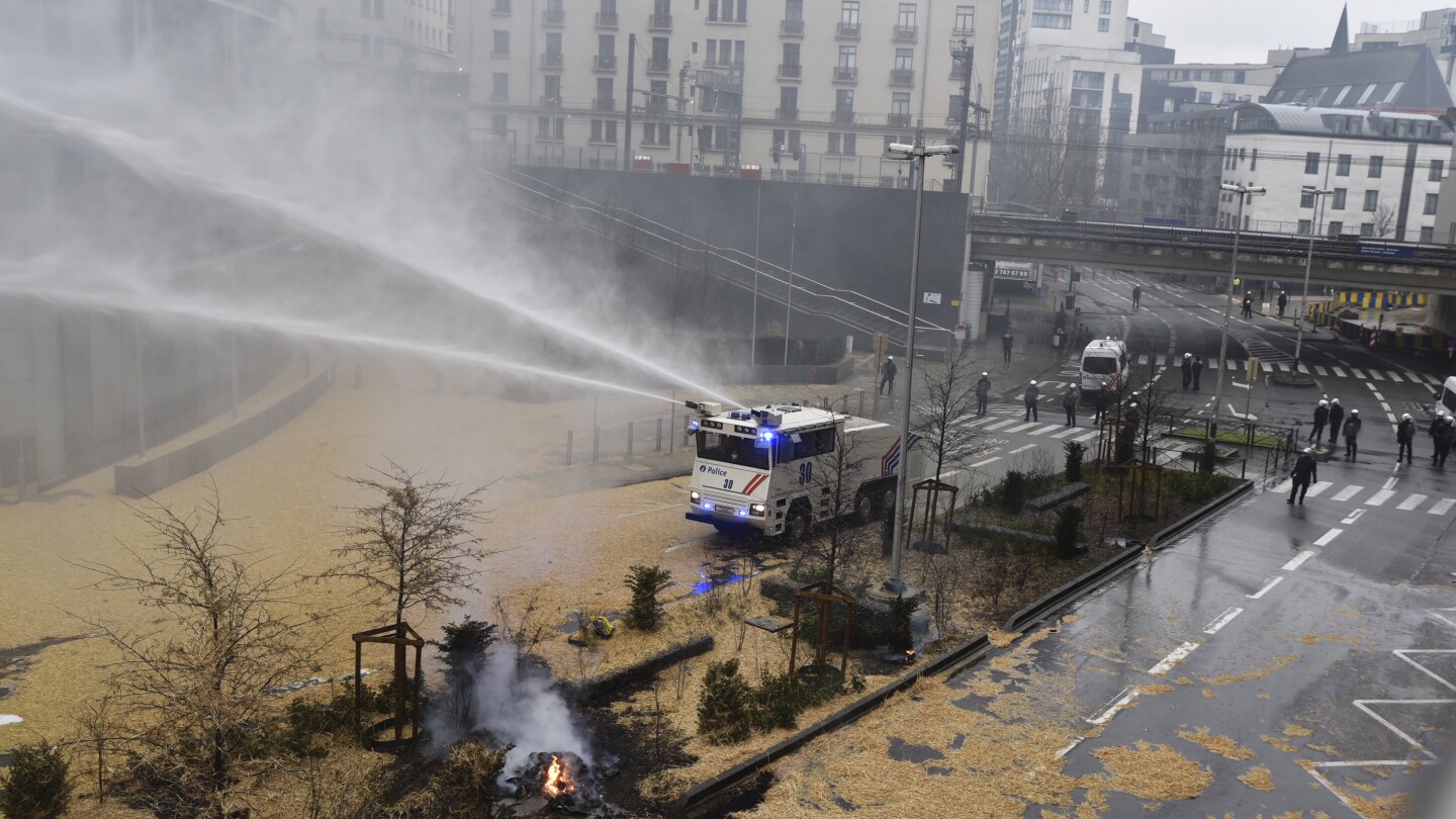 抗議している農家は、新しい権力を示すためにEU基地の近くでブリュッセル警察に液体の肥料を振りかけます。