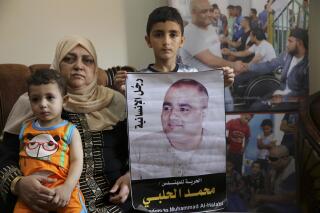 FILE - Amal el-Halabi holds her grandson Fares while her grandson Amro, 7, holds a picture of his father Mohammed el-Halabi, Gaza director of the international charity World Vision, who was convicted by an Israeli court of diverting sums to Hamas, at his family house in Gaza City, Aug. 8, 2016. An Israeli court has sentenced el-Halabi to 12 years in prison after he was found guilty earlier this year of several terrorism charges in a high-profile case in which independent probes found no evidence of wrongdoing.(AP Photo/Adel Hana, File)
