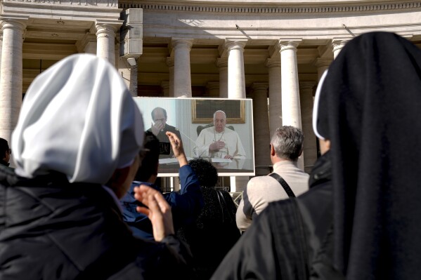 Nuns look at Pope Francis on a giant monitor set up in St. Peter's Square at The Vatican, Sunday, Dec. 3, 2023, as he blesses the faithful gathered in the square for the traditional Angelus noon prayer. Francis skipped his weekly Sunday appearance at a window because suffering from a mild flu. (AP Photo/Andrew Medichini)
