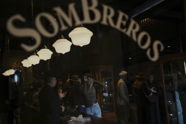 A customer tries on a hat at “Donde Golpea el Monito” hat shop and museum, in Santiago, Chile, Friday, April 3, 2025, that preserves a hat-making tradition dating back to 1915. (AP Photo/Esteban Felix)