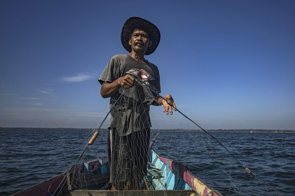 Erwin, a fisherman, uses a net to fish in the waters off Tanah Kuning, near the site for the future development of the Kalimantan Industrial Park Indonesia, in North Kalimantan, Indonesia on Thursday, Aug. 24, 2023. "We are looking for fish further and further away from the beach because there are lots of ships in the area driving fish away," said Erwin, who like many Indonesians uses only one name. (AP Photo/Yusuf Wahil)