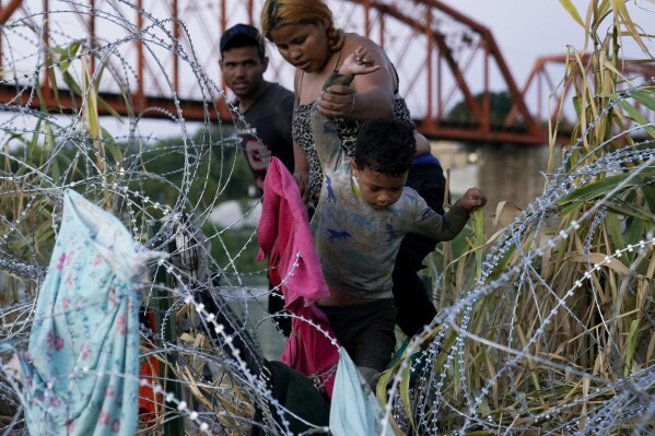 Migrants climb over concertina wire after they crossed the Rio Grande and entered the U.S. from Mexico, Saturday, Sept. 23, 2023, in Eagle Pass, Texas. (AP Photo/Eric Gay)