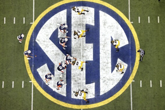 FILE - Auburn quarterback Nick Marshall (14), left, takes the snap from Auburn center Reese Dismukes (50) as the Auburn offense operates against Missouri on the SEC logo during the first half of Auburn's 59-42 win over Missouri in the SEC Championship at the Georgia Dome, Saturday, Dec. 7, 2013, in Atlanta, Ga. Southeastern Conference and Pac-12 officials are expected to provide the final approval of a $2.8 billion plan that will settle antitrust claims and set the stage for college athletes to start sharing the billions of dollars flowing to their schools. (AP Photo/Atlanta Journal-Constitution, Jason Getz, File)