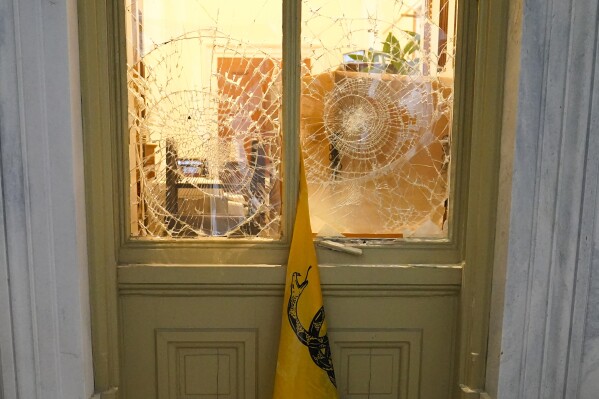 A flag hangs between broken windows after then-President Donald Trump supporters tried to break through police barriers outside the U.S. Capitol, Jan 6, 2021. (AP Photo/John Minchillo, File)