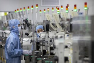 FILE - In this May 14, 2020, file photo, employees wearing protective equipment work at a semiconductor production facility for Renesas Electronics during a government organized tour for journalists in Beijing. China has announced tax breaks to spur growth of its semiconductor industry following U.S. sanctions that cut off access to American processor chips for tech giant Huawei and some other companies. (AP Photo/Mark Schiefelbein, File)