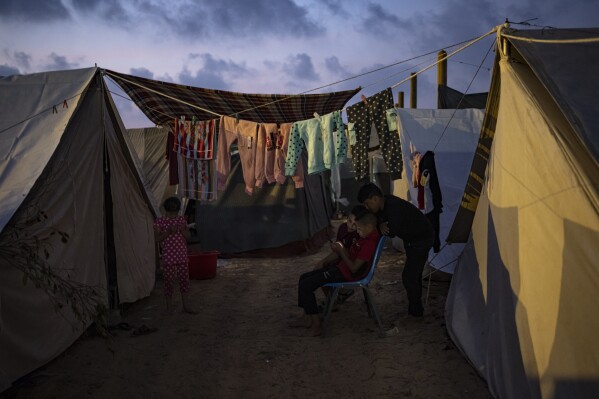 FILE - Palestinian kids, who were displaced by the Israeli bombardment of the Gaza Strip, watch a phone in a UNDP-provided tent camp in Khan Younis, Gaza Strip, Wednesday, Nov. 1, 2023. While journalists' access to the war in Gaza is limited, a flood of video from all sorts of sources documents what is — and isn't — going on. (AP Photo/Fatima Shbair, File)