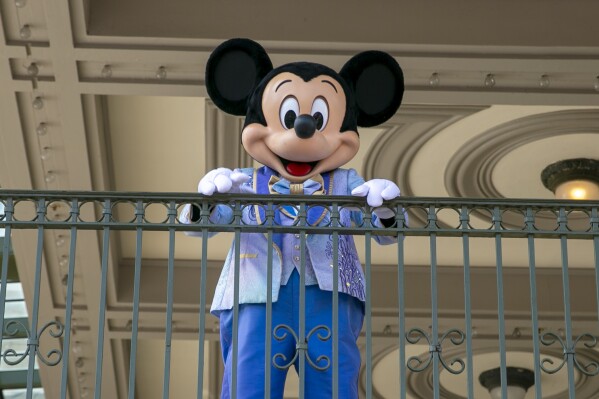 FILE - An actor dressed as Mickey Mouse greets visitors at the entrance to Magic Kingdom Park at Walt Disney World Resort, April 18, 2022, in Lake Buena Vista, Fla. Winnie the Pooh and Mickey Mouse have recently entered the public domain, making it possible for artists to use them freely. (AP Photo/Ted Shaffrey, File)