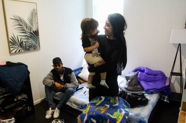 Barbara Peraza-Garcia holds her 2-year-old daughter, Frailys, while her partner Franklin Peraza sits connected their furniture successful their 'micro apartment' successful Seattle connected Monday, March 11, 2024. (AP Photo/Manuel Valdes)
