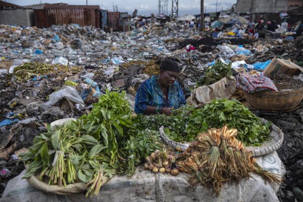 A woman selling greens waits for customers in the Croix des Bosalles market in Port-au-Prince, Haiti, Sept. 22, 2021. The floor of the market is thick with decomposing trash and, in some places, small fires of burning trash. (AP Photo/Rodrigo Abd)