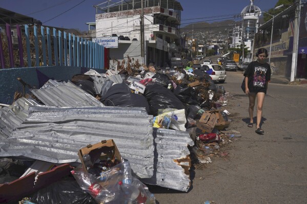 FILE - A resident walks past debris more than two weeks after Hurricane Otis hit Acapulco, Mexico, as a Category 5 storm, Nov. 13, 2023. Mexican President Andrés Manuel López Obrador spoke Wednesday, Dec. 20, 2023, about the recovery of Acapulco after Hurricane Otis smashed into the resort on Oct. 25, killing 52 people. But some residents still don’t have running water, sewage treatment is still deficient, tons of garbage and debris remain in the streets, and few hotels are fully open. (AP Photo/Marco Ugarte, File)