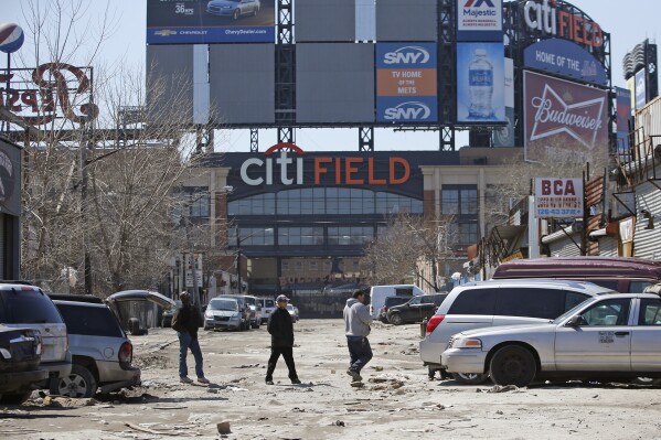 FILE - In this April 2, 2015 photo, workers cross an unpaved street adjacent to Citi Field, home to the New York Mets baseball team in the Willets Point section of the Queens borough of New York. New York City officials approved a plan Thursday, April 11, 2024, to build a 25,000-seat stadium for Major League Soccer’s New York City Football Club next to the New York Mets’ stadium, Citi Field. The $780 million soccer stadium, expected to open in 2027, will anchor a 23-acre redevelopment project in the neighborhood known as Willets Point that will also include housing, a new public school, retail stores and a hotel. (AP Photo/Kathy Willens, File)