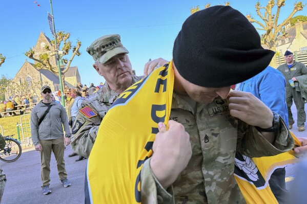 Joint Chiefs Chairman Gen. Mark Milley signs a 101st Airborne Division flag for Staff Sgt. Wolfe in the town square at Sainte-Mere-Eglise in Normandy, France, June 4, 2023. The village hosts an annual D-Day celebration honoring the units who parachuted in on June 6, 1944, launching the liberation of France. This was Milley's last visit here as a soldier. (AP Photo/Tara Copp)