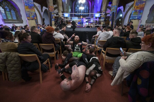 Un grupo de seis hombres sale del ring durante un espectáculo de Kingdom Wrestling en la iglesia de San Pedro en Shipley, el sábado 29 de marzo de 2025. (Foto AP/Jon Super)