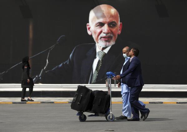 FILE - Passengers walk to the departures terminal of Hamid Karzai International Airport in Kabul, Afghanistan, on Saturday, Aug. 14, 2021, past a mural of President Ashraf Ghani, as the Taliban offensive encircled the capital. On the eve of the anniversary of the Taliban takeover of Kabul, Afghanistan's former president on Sunday, Aug. 14, 2022, defended what he said was a split-second decision to flee, saying he wanted to avoid the humiliation of surrender to the insurgents. (AP Photo/Rahmat Gul, File)