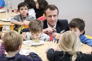 FILE - In this Jan.18, 2019 file photo, French President Emmanuel Macron meets pupils as he visits a school canteen in Saint-Sozy, southwestern France. By taking meat off the menu at school canteens, the Green Party mayor of Lyon has kicked up a storm of protest and debate in a country increasingly asking questions about the environmental costs of its meaty dietary habits. With a meatless four-course meal that Lyon City Hall says will be quicker and easier to serve to children who must be kept socially distanced while eating lunch to avoid coronavirus infections. (Ludovic Marin/Pool Photo via AP, FILE)