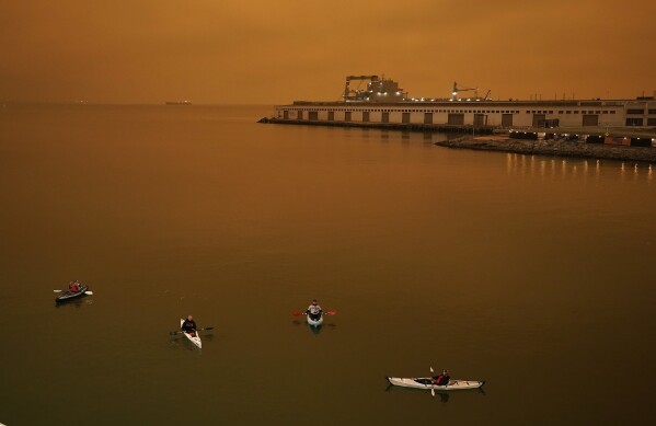 FILE - People in kayaks paddle in McCovey Cove outside Oracle Park in San Francisco during a baseball game between the San Francisco Giants and the Seattle Mariners on Sept. 9, 2020. As Earth's climate continues to change from heat-trapping gases spewed into the air, ever fewer people are out of reach from the billowing and deadly fingers of wildfire smoke, scientists say. (AP Photo/Tony Avelar, File)