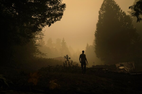 FILE - A man holds a jug of water he used to douse hot spots at a home destroyed by the the Riverside Fire, Sept. 11, 2020, in Estacada, Ore. Dozens of Oregon wineries and vineyards have sued PacifiCorp over the deadly 2020 wildfires that ravaged the state, alleging that the utility's decision to not turn off power during the Labor Day windstorm contributed to blazes whose smoke and soot damaged their grapes and reduced their harvest and sales. (AP Photo/John Locher, File)