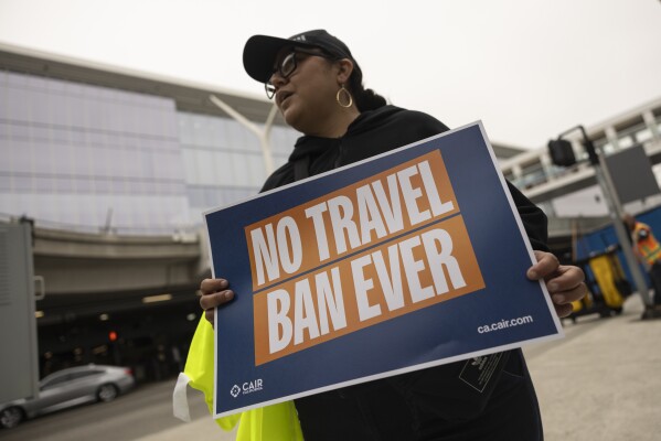 A demonstrator holds a poster during a protest against new travel ban announced last week by President Donald Trump, at the Tom Bradley International Terminal at Los Angeles International Airport, Monday, June 9, 2025, in Los Angeles. (AP Photo/Etienne Laurent)
