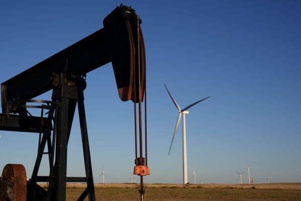 Pumpjacks operate in the foreground while wind turbines at the Buckeye Wind Energy wind farm rise in the distance, Sept. 30, 2024, near Hays, Kan. (AP Photo/Charlie Riedel, File)