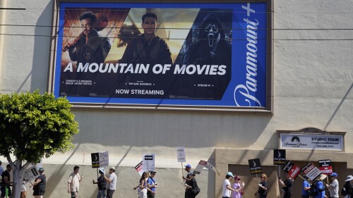 An advertisement for streaming service Paramount+ appears above striking writers and actors at rally outside Paramount studios in Los Angeles on Friday, July 14, 2023. This marks the first day actors formally joined the picket lines, more than two months after screenwriters began striking in their bid to get better pay and working conditions. (AP Photo/Chris Pizzello)