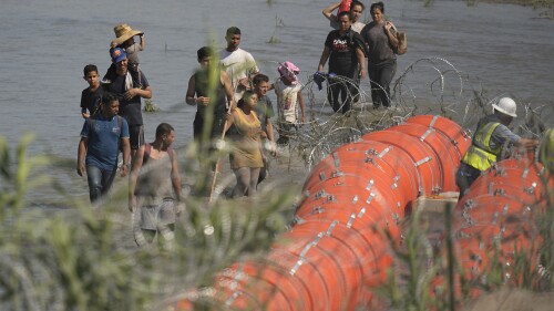 Migrants trying to enter the U.S. from Mexico approach the site where workers are assembling large buoys to be used as a border barrier along the banks of the Rio Grande in Eagle Pass, Texas, Tuesday, July 11, 2023. (AP Photo/Eric Gay)