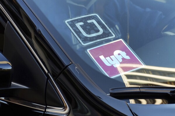 FILE - A ride share car displays Lyft and Uber stickers on its front windshield in downtown Los Angeles, Jan. 12, 2016. The ride-hailing companies Uber and Lyft said they will delay their plans to stop operating in Minneapolis after city officials decided Wednesday, April 11, 2024, to delay an ordinance requiring increased pay rates for drivers. (AP Photo/Richard Vogel, File)