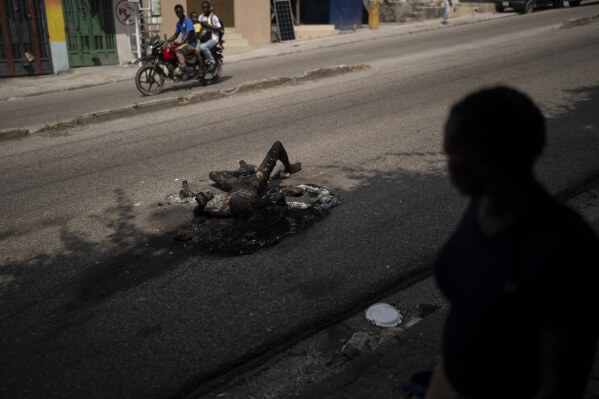 EDS NOTE: GRAPHIC CONTENT - People pass by the body of a man who was killed and set on fire in the Delmas area of Port-au-Prince, Haiti, on June 5, 2023. (AP Photo/Ariana Cubillos)